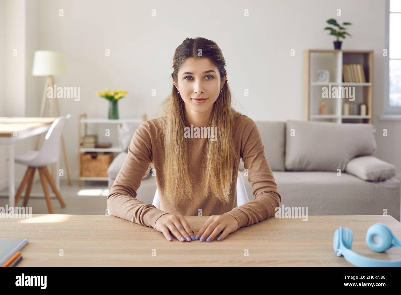 Porträt einer netten, freundlichen jungen Frau, die Webcam anschaut, während sie zu Hause im Wohnzimmer sitzt. Stockfoto
