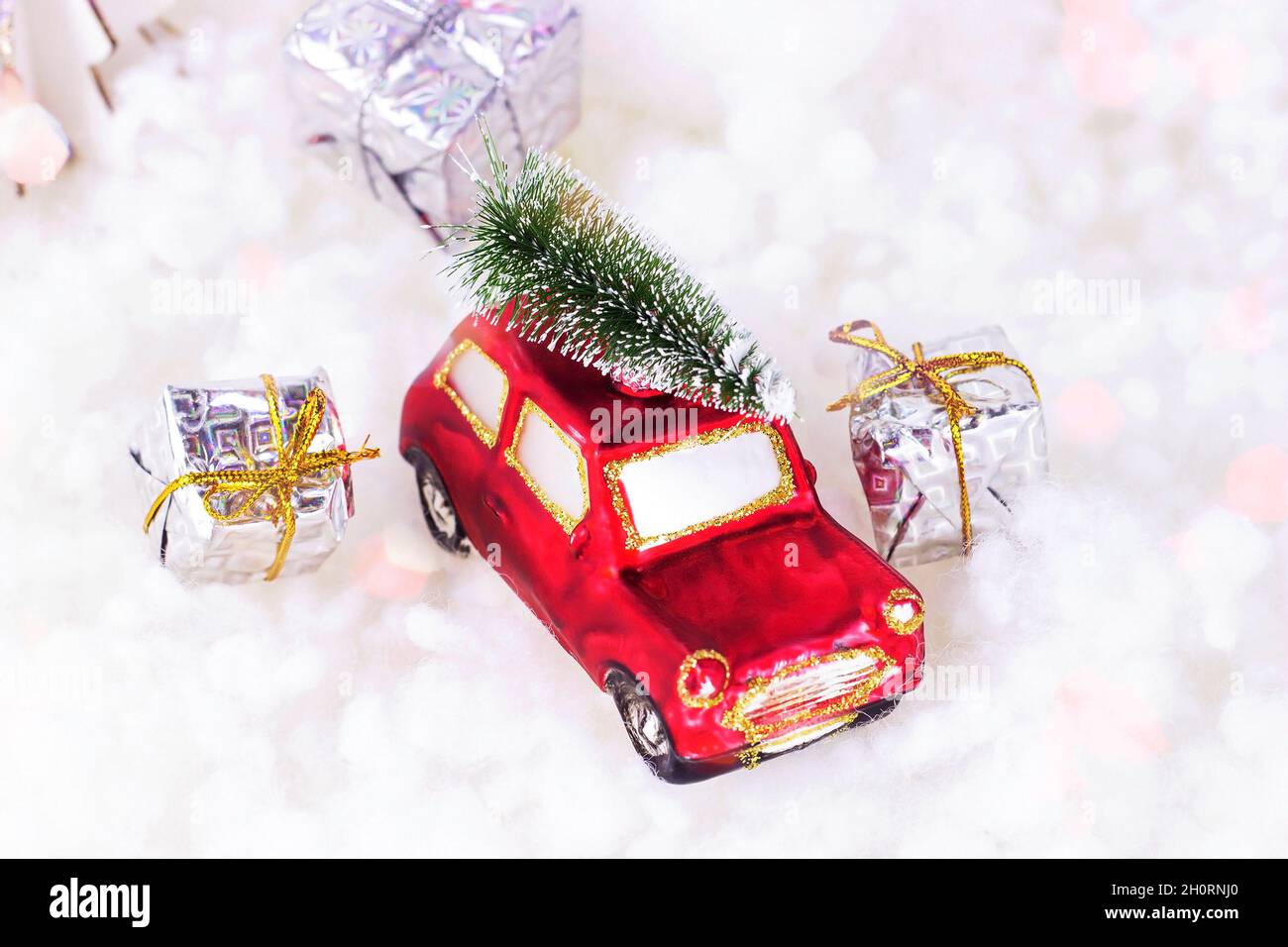 Kleines rotes Retro-Spielzeugauto mit grüner Tanne auf der Oberseite und präsentiert sich auf weißem künstlichen Schnee Hintergrund. Weihnachts- und Neujahrsfeiertage Stockfoto