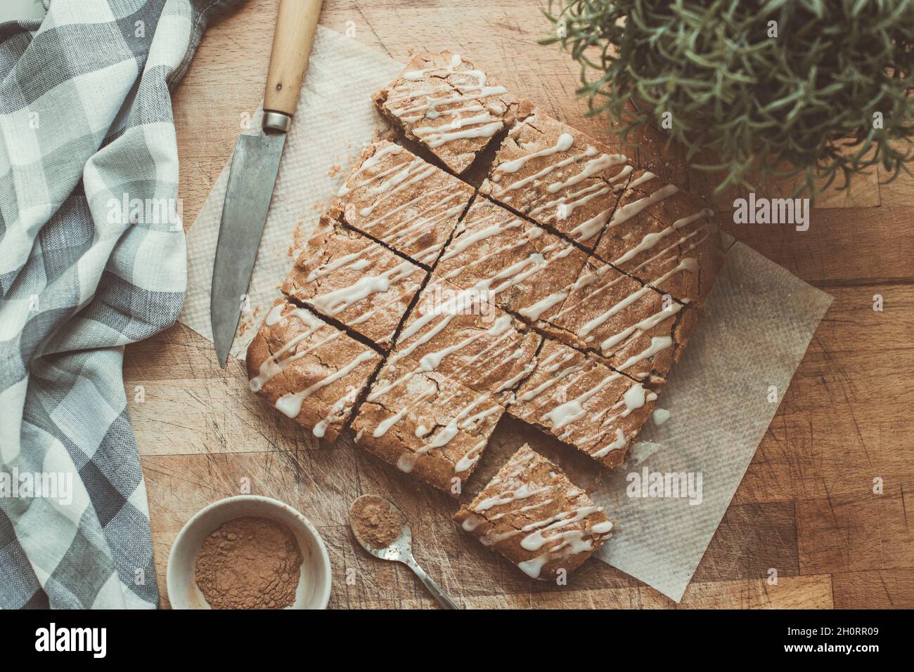 Selbstgemachte Karamell-Blondie-Bars auf einem Holztisch mit einem Messer, einem Geschirrtuch und einer Topfpflanze Stockfoto
