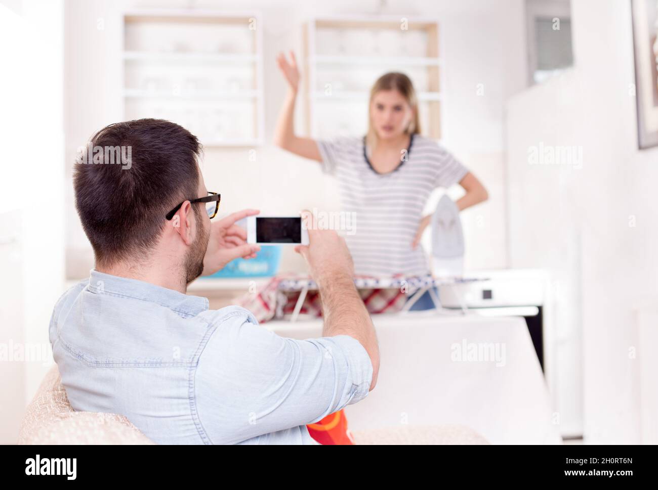 Hübscher junger Mann, der Spaß hat, seine zornige Freundin beim Bügeln und bei der Arbeit festzuhalten Stockfoto