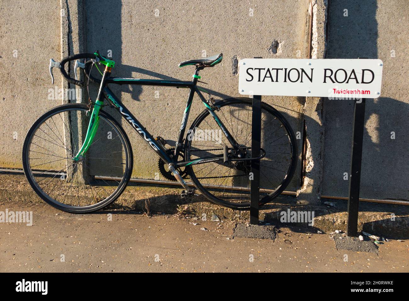 Ein Pendlerfahrrad, das sich an einem Schild für die Station Road in Twickenham, in der Nähe des Hauptbahnhofs mit Zügen nach London und anderen Zielen, versperrte. VEREINIGTES KÖNIGREICH. (127) Stockfoto