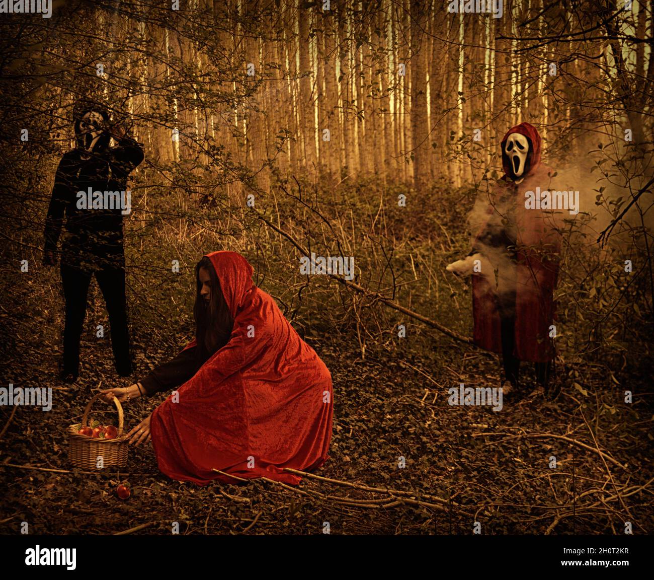 Kleine rote Reithaube mit maskierter Person in Schwarz, die dahinter steht. Schuss in schattigen Wäldern. Stockfoto