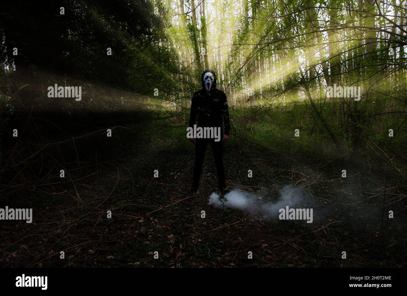 Beängstigender Mann, der mit einer weißen Maske im Wald steht. Stockfoto