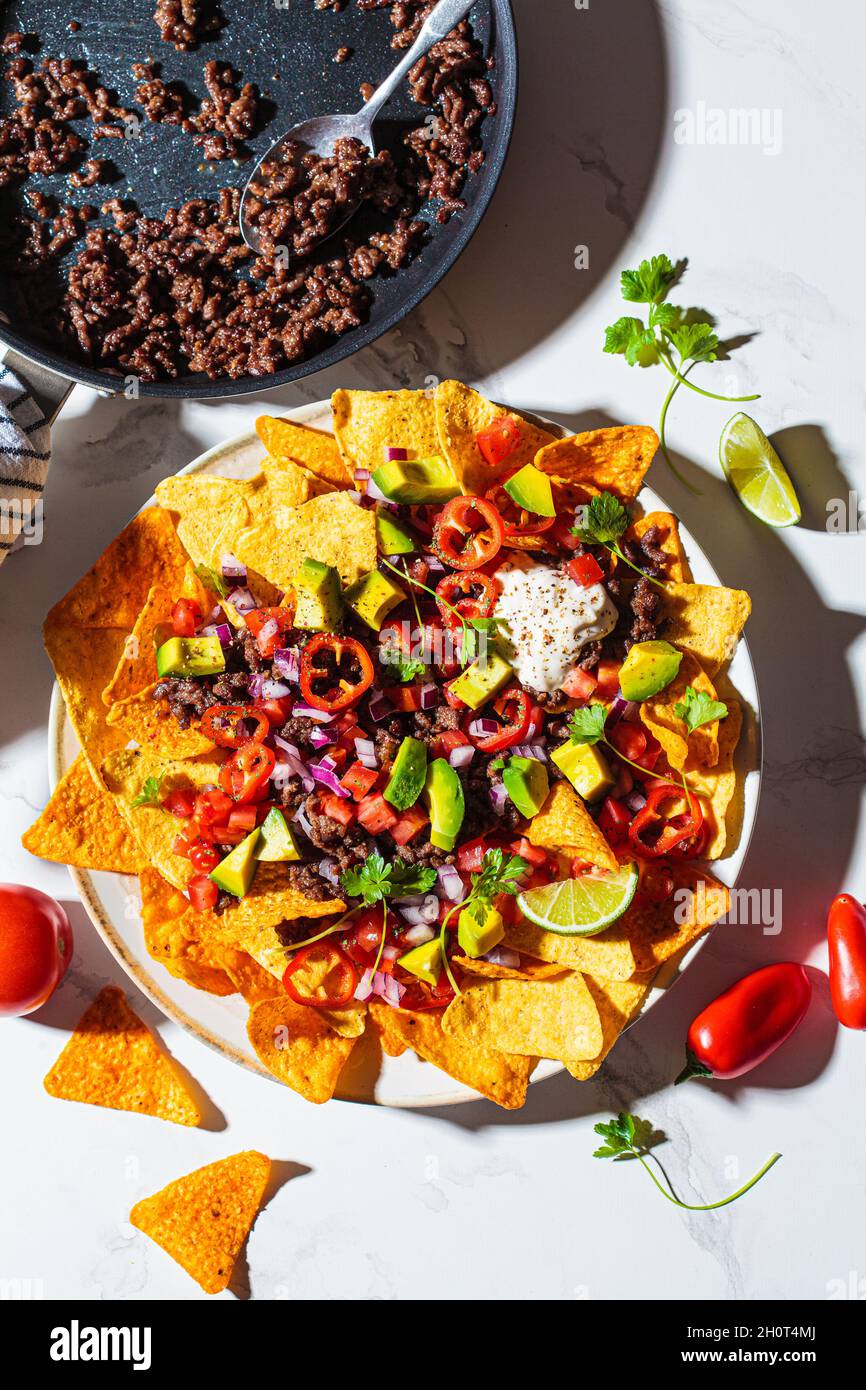 Mexikanisches Speisekonzept. Mais-Nachos-Chips mit Avocado, Pfeffer, Salsa und gegrilltem Hackfleisch auf weißem Teller, weißer Marmorhintergrund, Draufsicht. Stockfoto