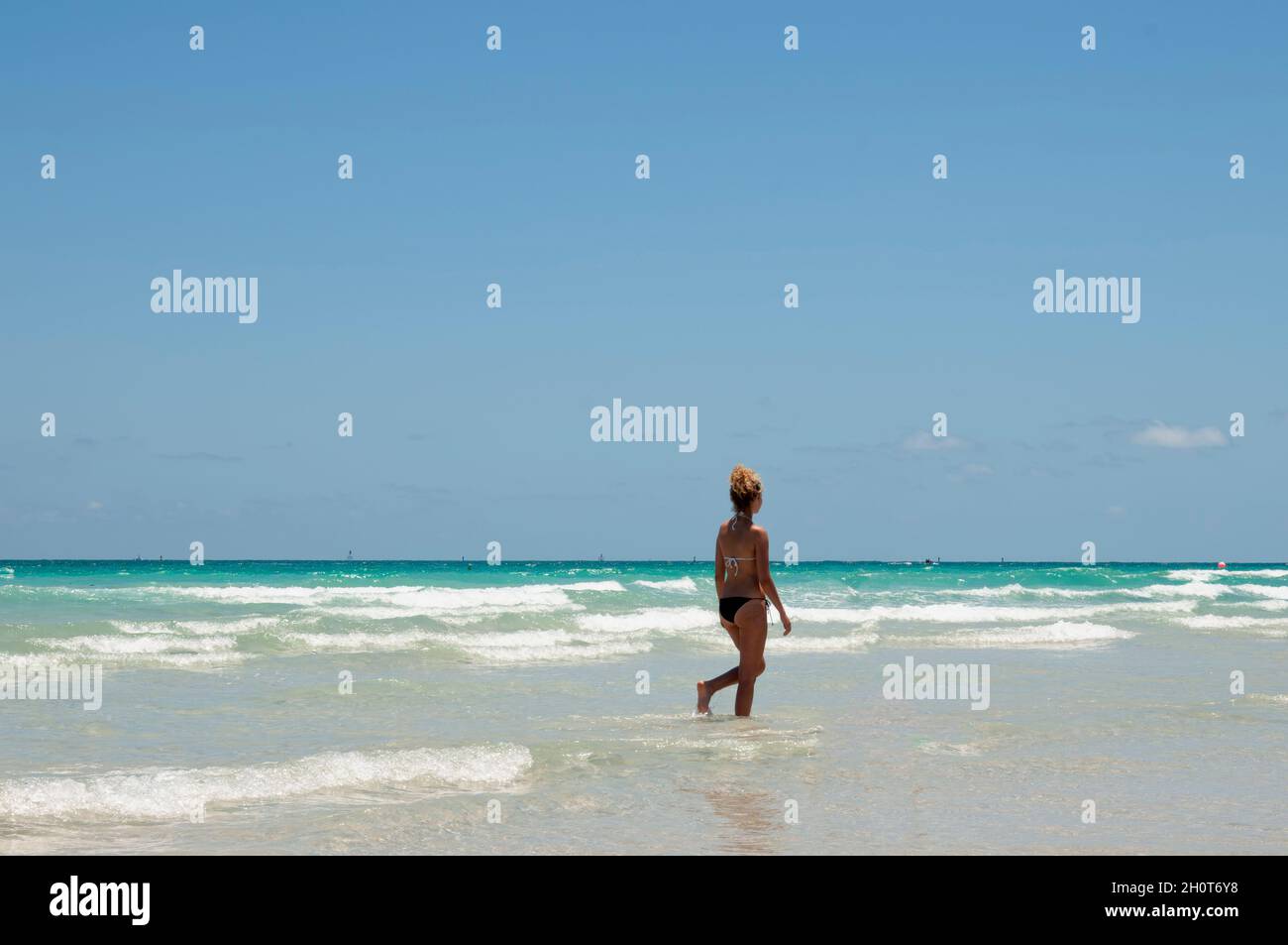 Eine Frau mit einem fitgen Körper, die einen Bikini trägt und an einem Sommertag mit wolkenlosem Himmel auf Miami Beach läuft Stockfoto