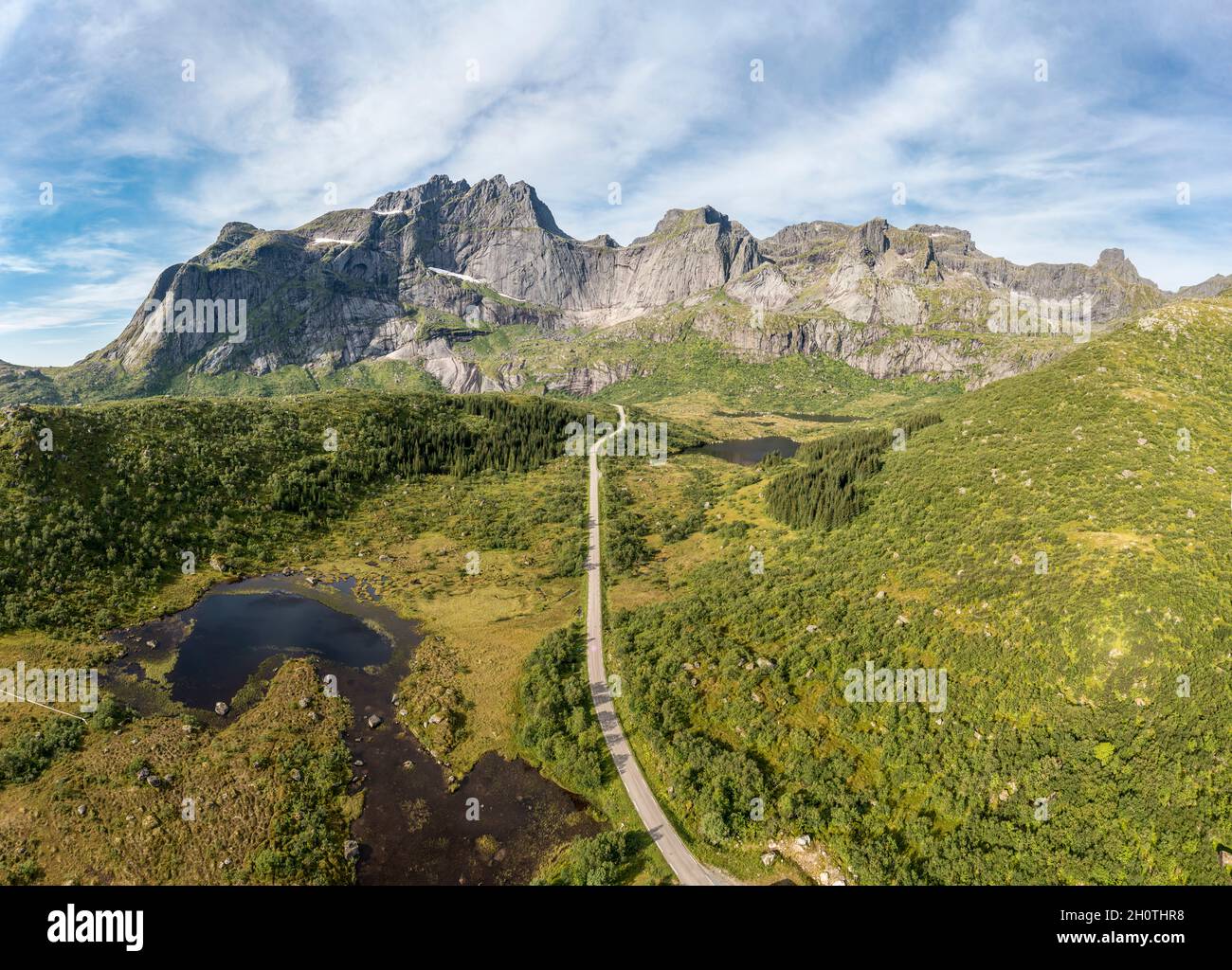 Panorama-Luftaufnahme der Straße in Bergkulisse, vorbei an Seen und Wiesen, Straße von E10 nach Dorf Nusfjord, Lofoten, Norwegen Stockfoto