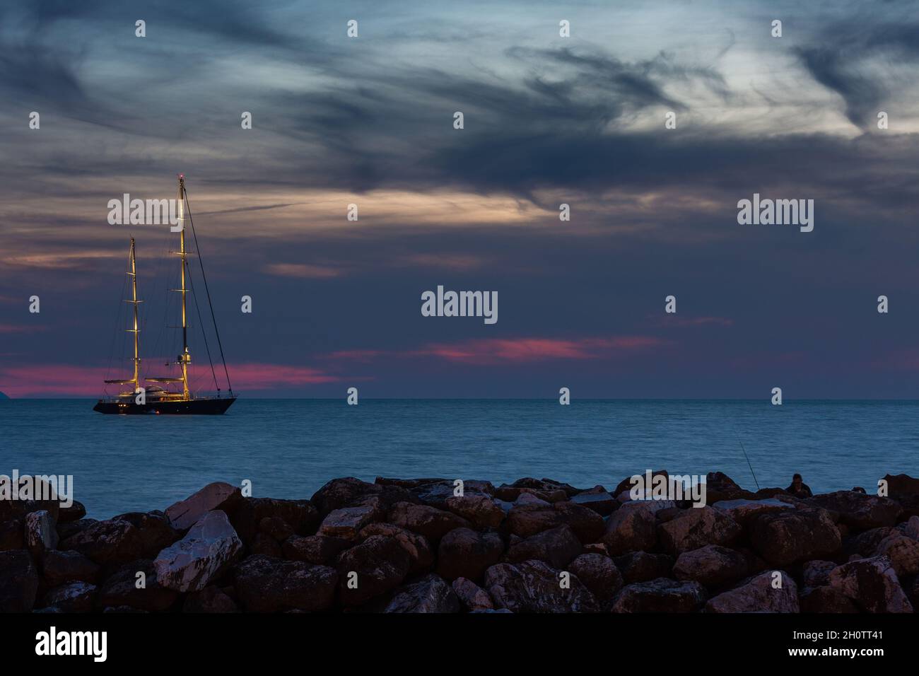 Segelschiff in der Dämmerung, Felsen im Vordergrund Stockfoto