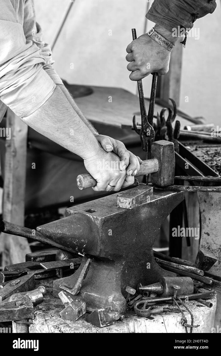 Die Hände von zwei Schmieden, die mit Hammer und Zange an einem Amboss arbeiten Stockfoto