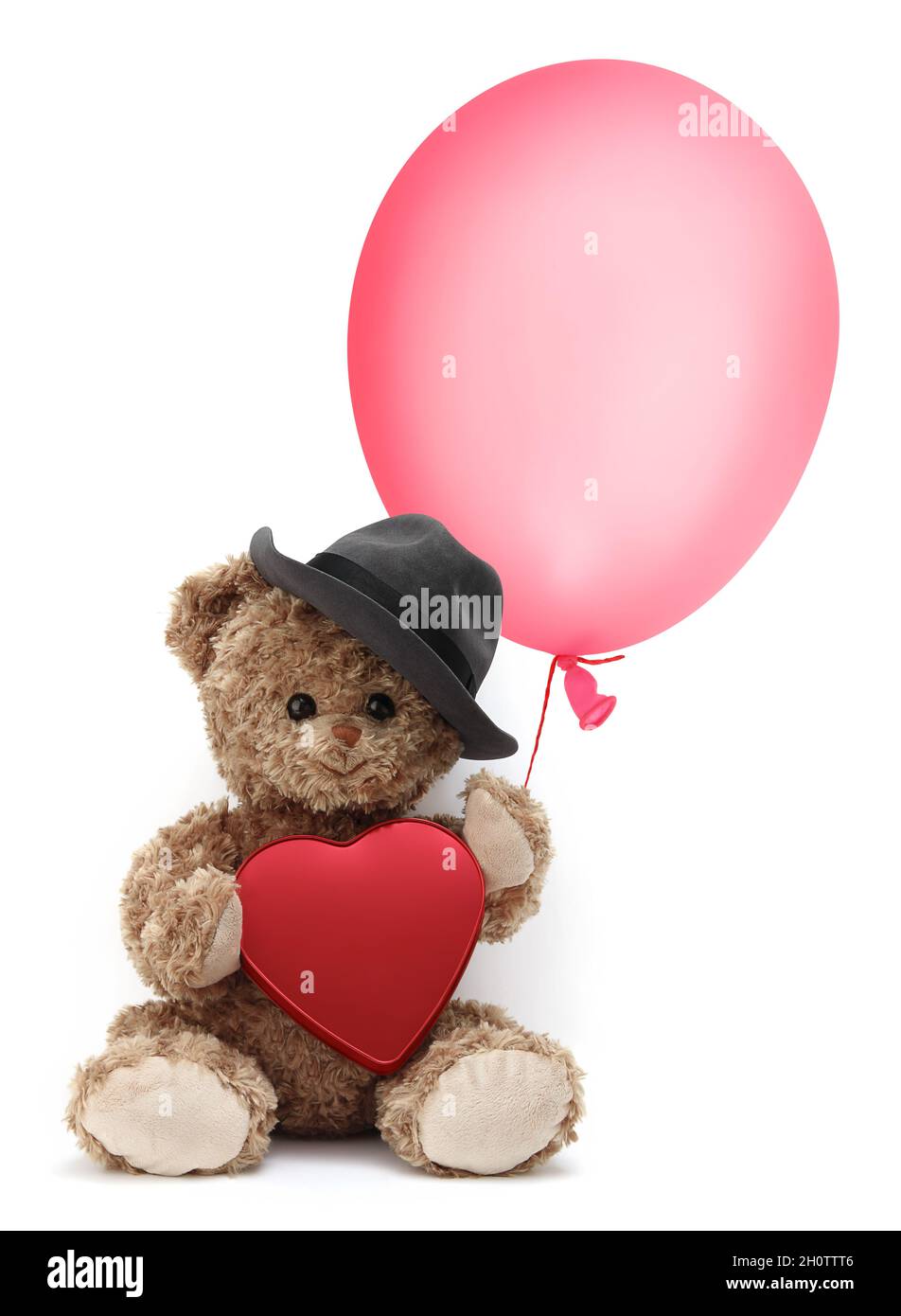 Der niedliche Teddybär trägt einen Hut und hält einen Ballon und ein rotes Herz, isoliert auf weißem Hintergrund Stockfoto