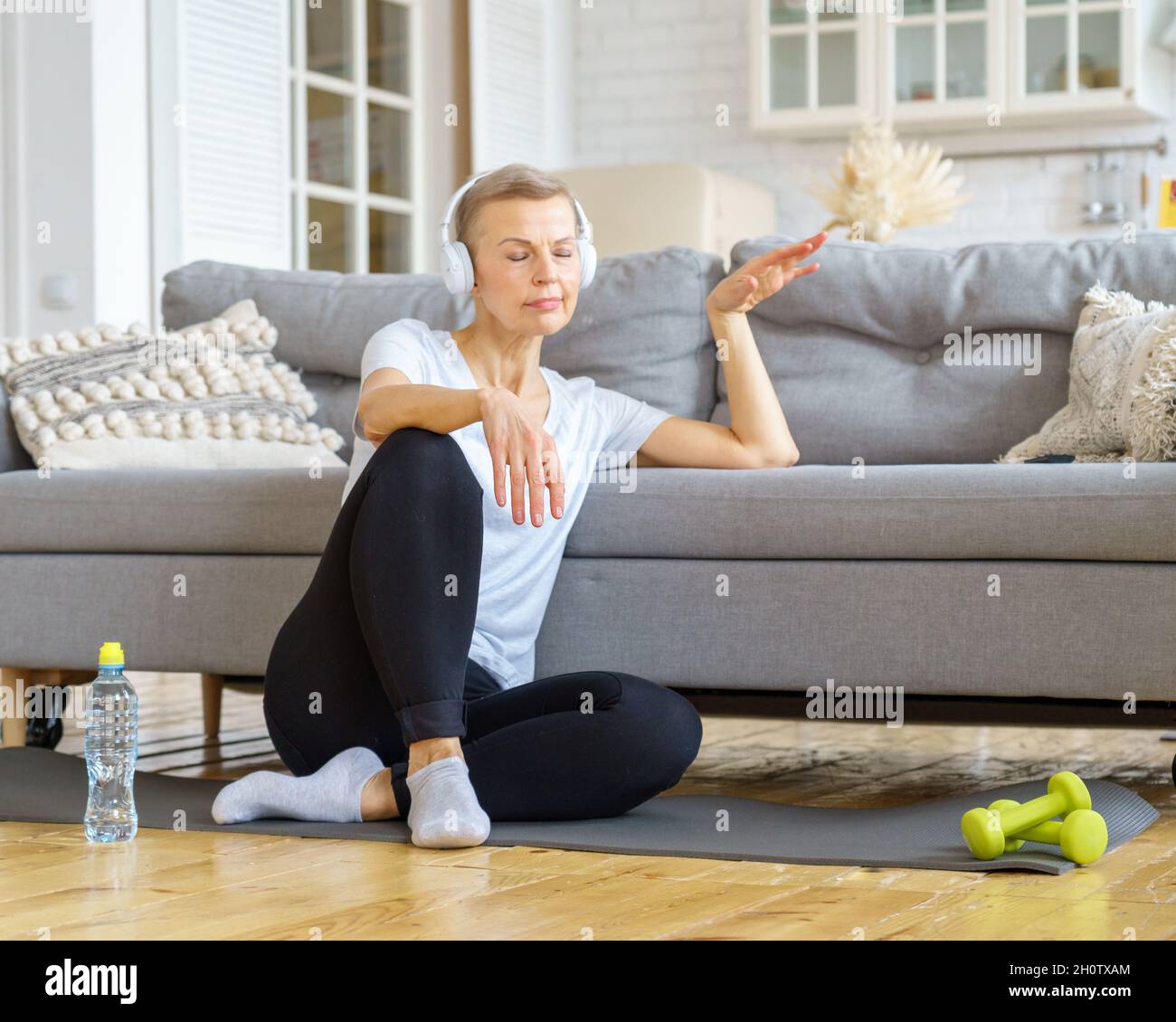 Alte Frau, die sich nach einer Fitnessaktivität zu Hause entspannt und Musik hört. Stressabbau Aktivitäten Stockfoto