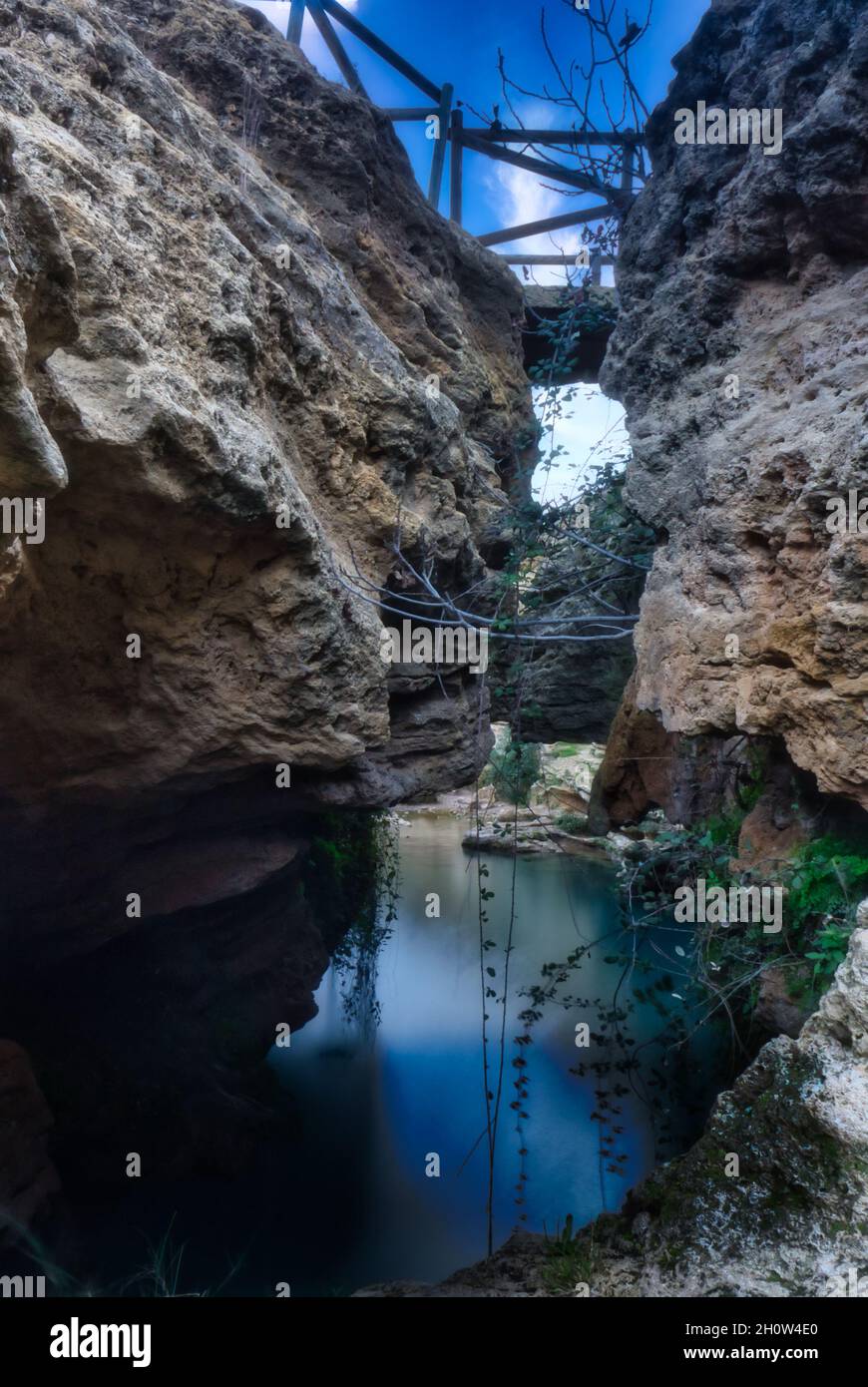 Faszinierender Blick auf eine Brücke zwischen felsigen Klippen über glänzendem Wasser unter einem blau bewölkten Himmel Stockfoto