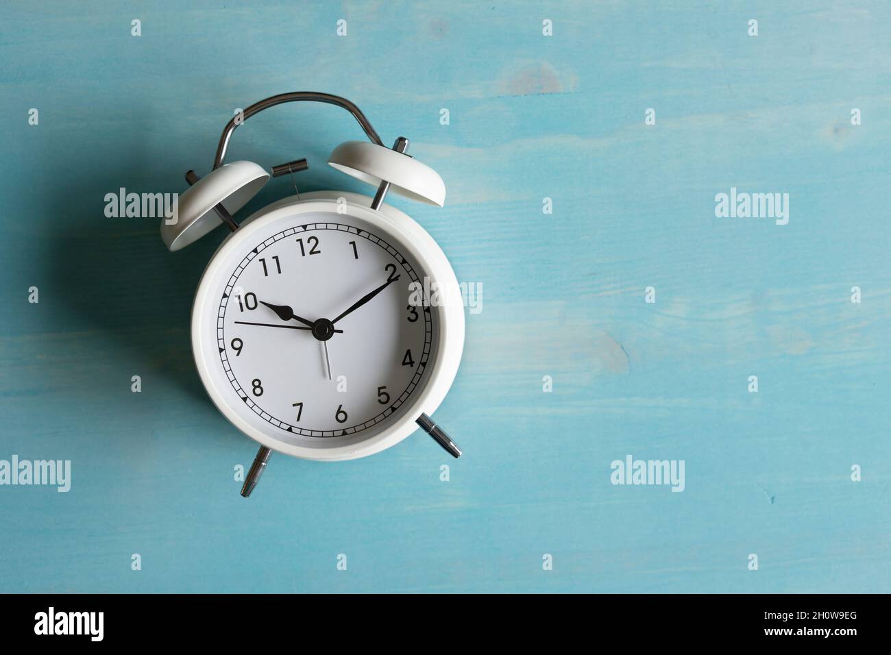 Kleiner weißer Retro-Wecker auf blauem Holzhintergrund mit Kopierfläche Stockfoto