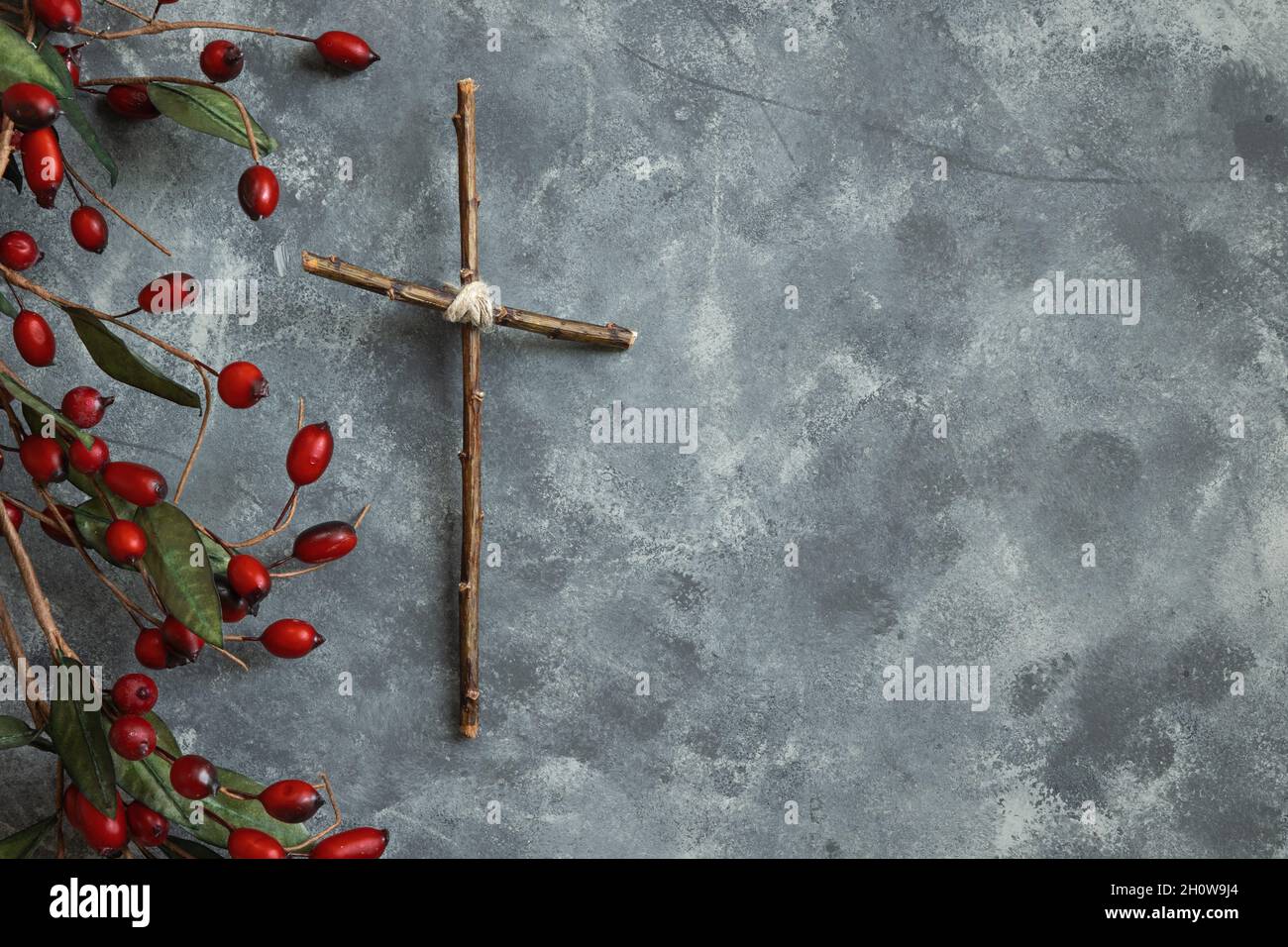 Einfaches Holzkreuz mit weihnachtlicher Holly-Beere-Bordüre auf grauem Hintergrund mit Kopierraum Stockfoto