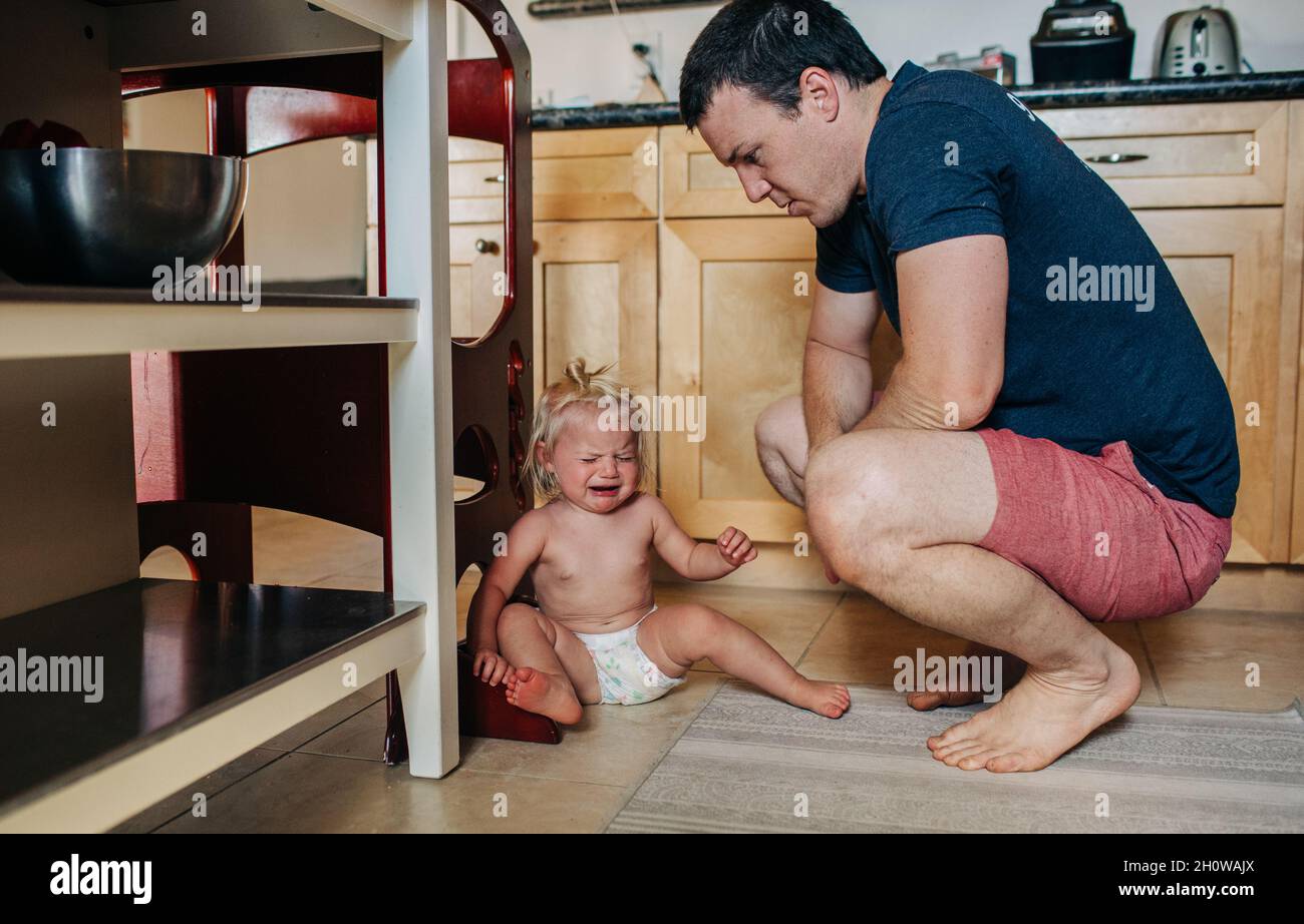 Papa blickt auf ein Mädchen mit einem abgediaperten Kleinkind, während er in der Küche weint Stockfoto