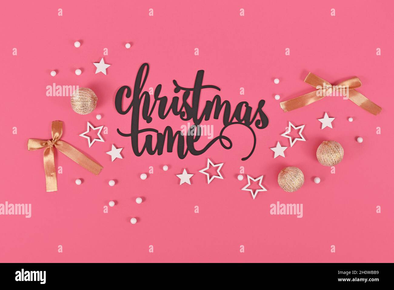 Schwarzer „Christmas Time“-Text neben goldener und weißer Kugel und Sternornamenten auf rosa Hintergrund Stockfoto