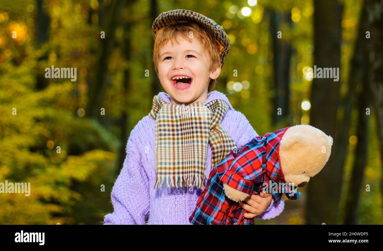 Herbstzeit. Kleiner Junge, der im Park mit Teddybär spielt. Glückliches Kind in warmen Kleidern, das im Herbstwald spazierengeht. Herbstmode für Kinder. Stockfoto