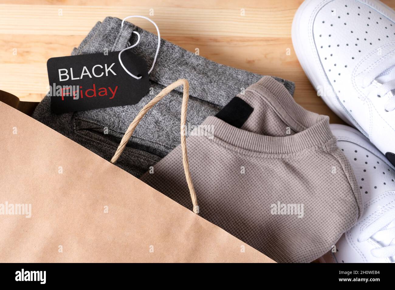 Stilvolle Herrenbekleidung in einer Papiertasche mit Schuhen mit einem schwarzen freitagsschild auf einem Holztisch. Stockfoto
