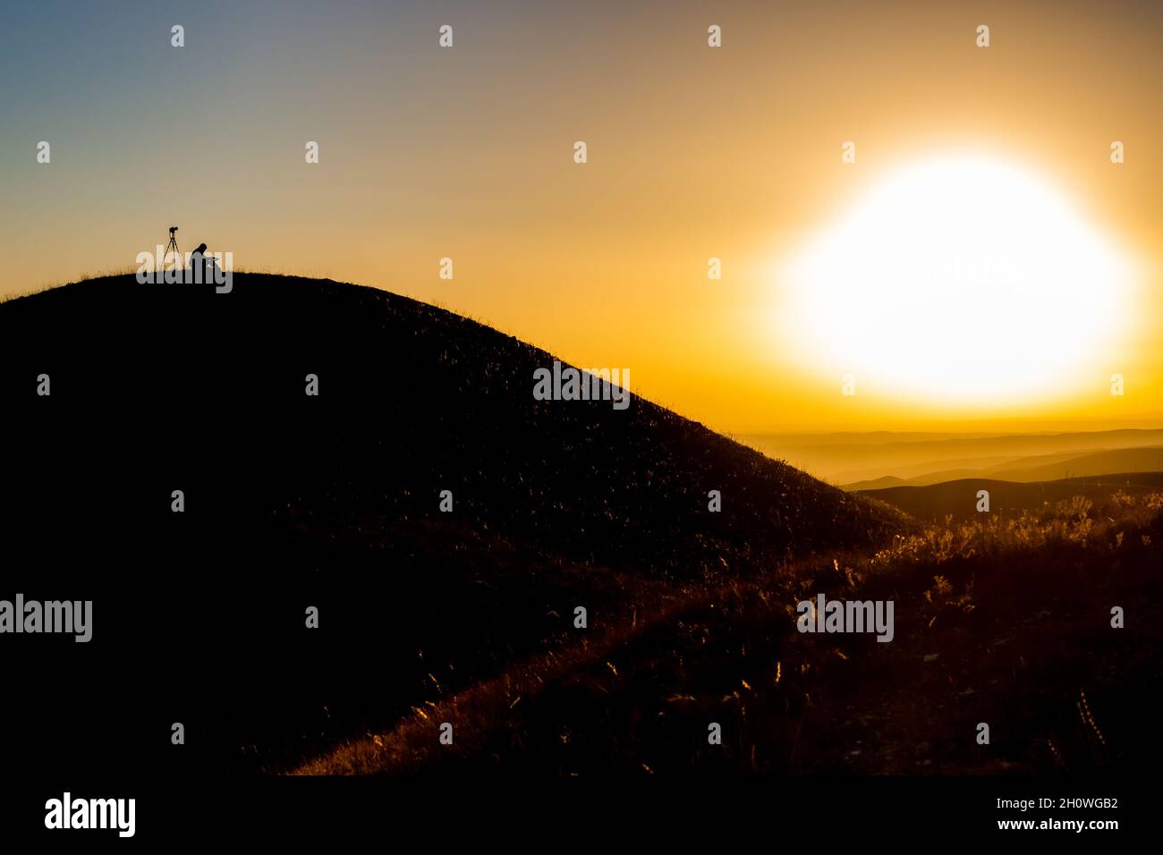 Fotograf beim Lesen und Entspannen am Hügel bei Sonnenuntergang Stockfoto