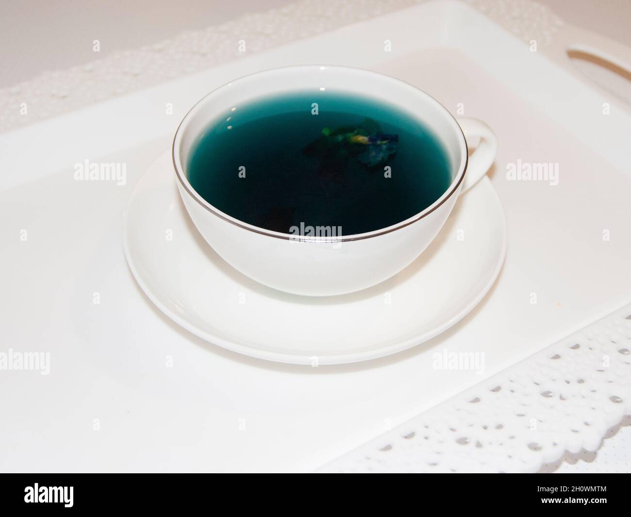 Die Stimmungsfarbe ist blau - blauer Tee in einem weißen Becher, der auf einer weißen Untertasse und einem weißen Tablett steht. Nützliche Getränke, heilende Eigenschaften. Phytotherapie. Te Stockfoto