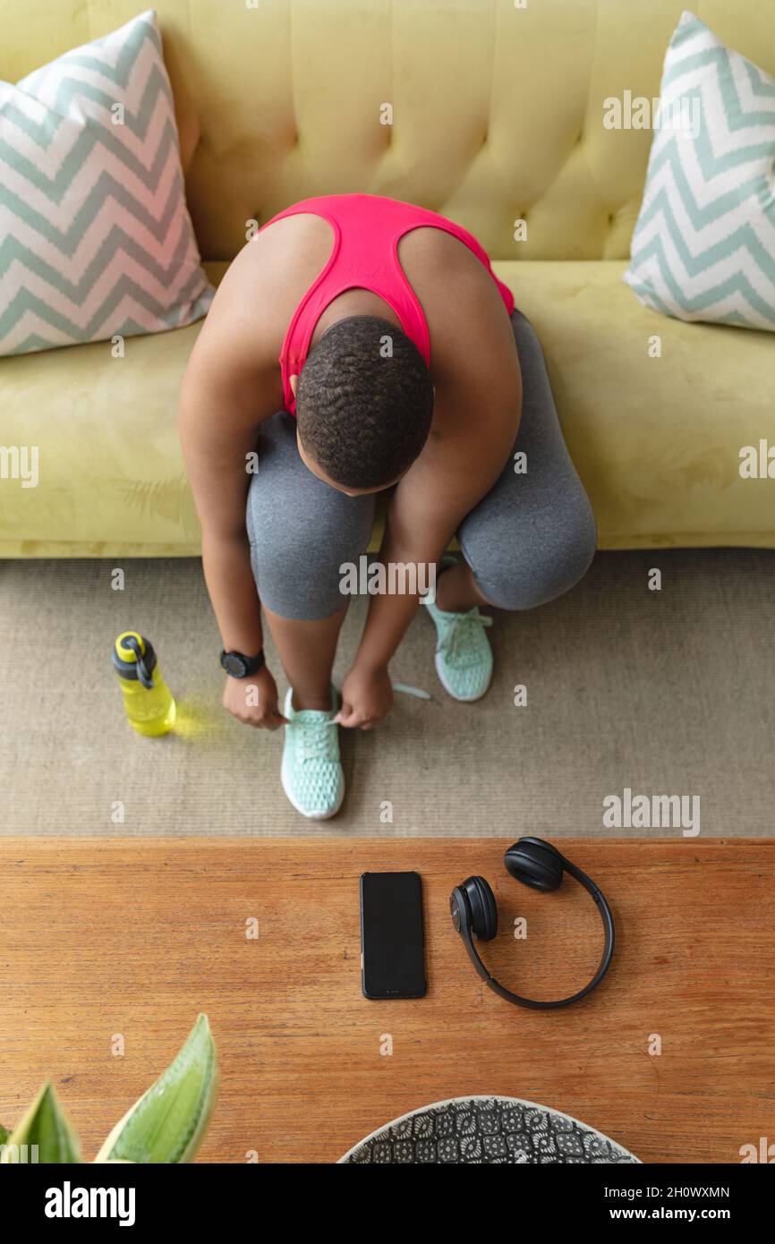 afroamerikanische Plus-Size-Frau in Sportkleidung sitzt auf dem Sofa und bindet Schuhe Stockfoto