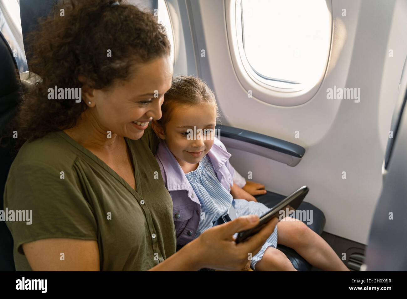 Lächelnde Frau mit ihrem Kind, das im Flugzeug sitzt und das Smartphone benutzt Stockfoto