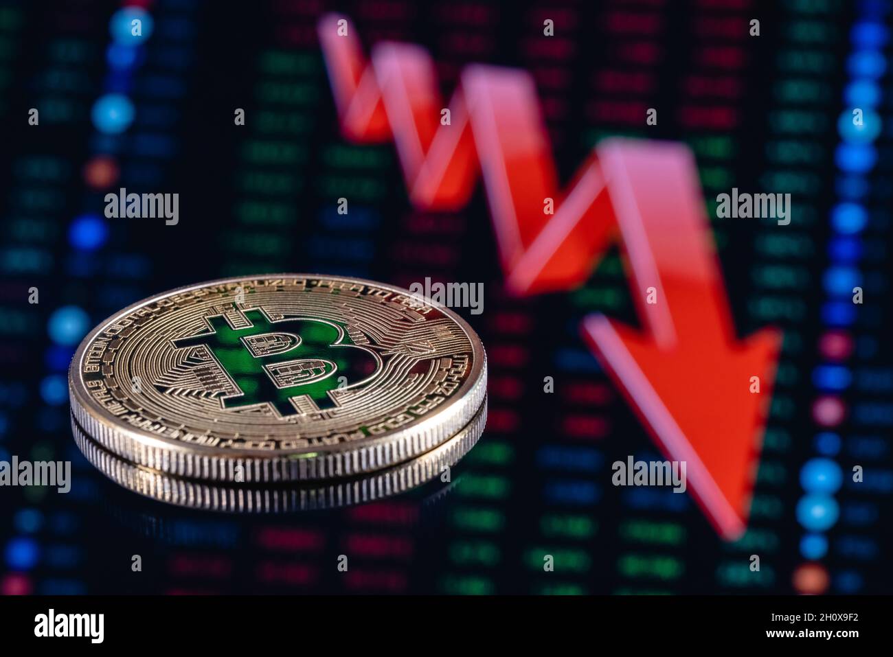 Bitcoin auf dem Hintergrund eines großen roten Pfeils, der nach unten zeigt. Das Konzept der sinkenden Bitcoin-Rate. Stockfoto