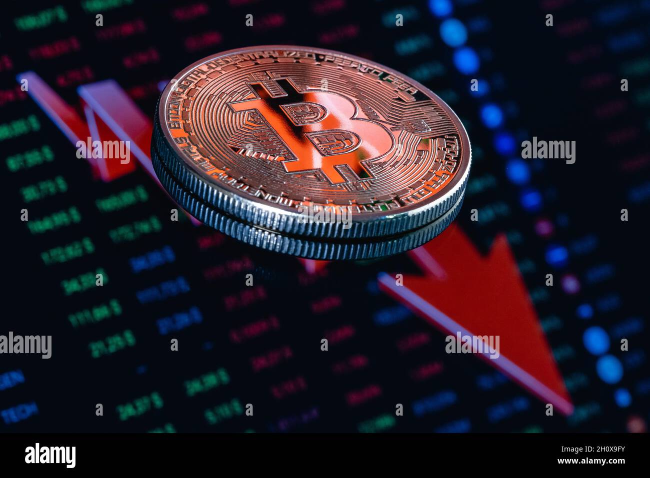 Bitcoin auf dem Hintergrund eines großen roten Pfeils, der nach unten zeigt. Das Konzept der sinkenden Bitcoin-Rate. Stockfoto