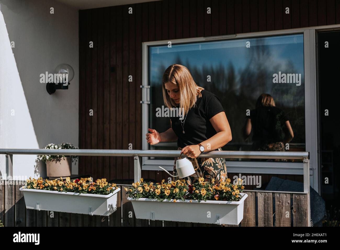 Frau Bewässerung Blumen auf Balkon Stockfoto
