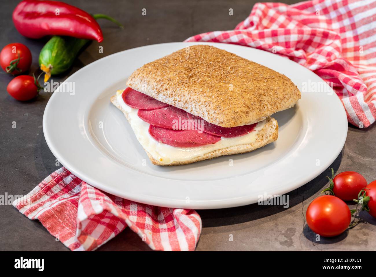 Salami- und Cheddar-Sandwich auf weißem Porzellanteller auf Steintisch Stockfoto