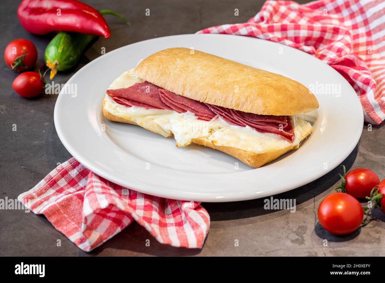 Salami- und Cheddar-Sandwich auf weißem Porzellanteller auf Steintisch Stockfoto