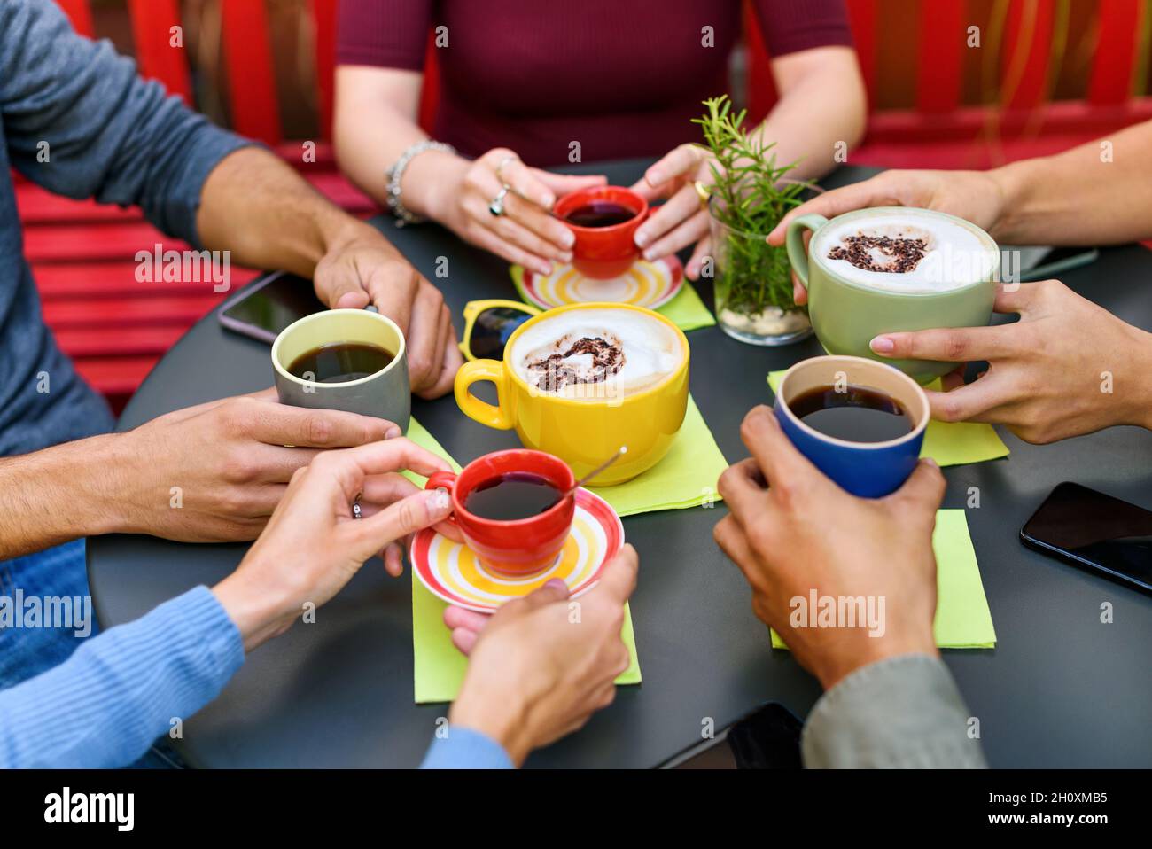 Von oben von Ernte unkenntlich Freunde sitzen an runden schwarzen Tisch und hält Tassen Kaffee und Cappuccino, während Zeit zusammen im Café zu verbringen Stockfoto