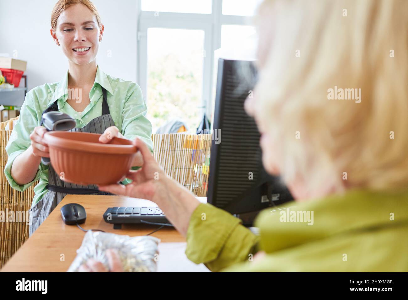 Frau, die beim Scannen des Barcodes an der Kasse des Gartencenters mit der Kassiererin bezahlt Stockfoto