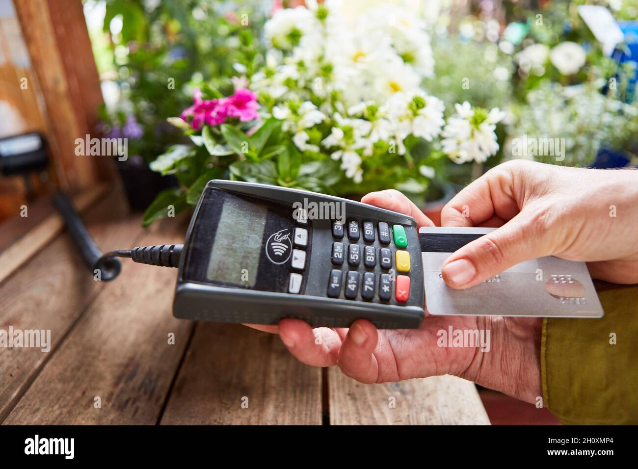 Der Kunde zahlt bargeldlos mit Kreditkarte an der Kasse im Blumenladen oder Geschäft Stockfoto