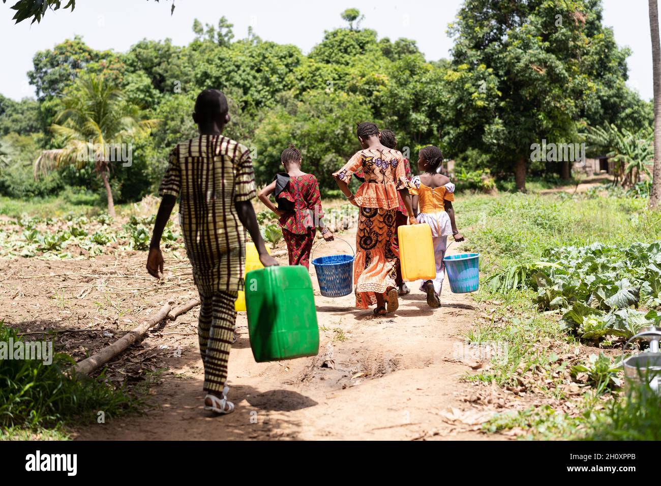 Eine Gruppe von müden schwarzafrikanischen Kindern im Schulalter, die mit dem Wassertragen aus dem Dorfbrunnen beschäftigt sind; Konzept der Kinderarbeit Stockfoto