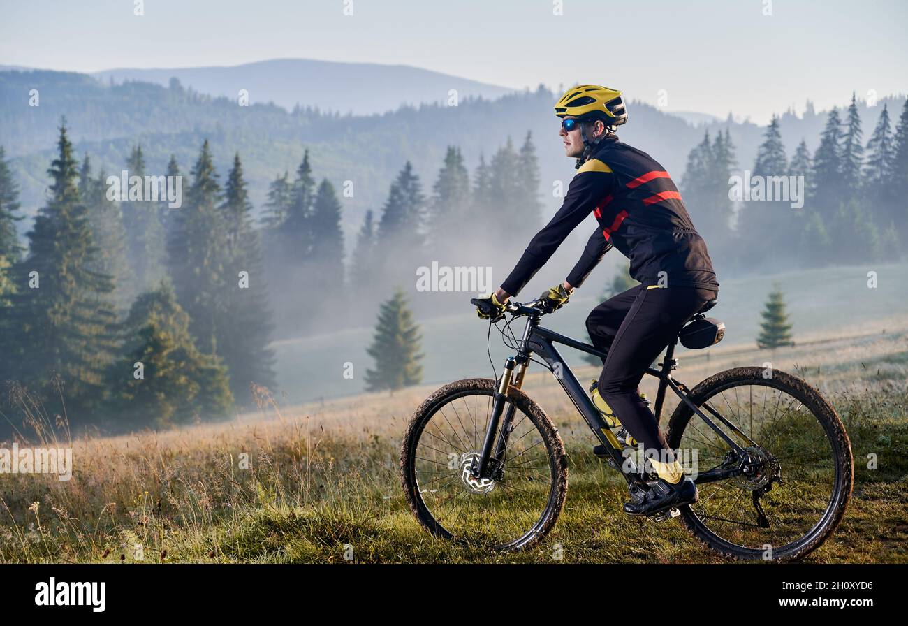 Mann Fahrradfahrer auf seinem Fahrrad in den Bergen in den frühen nebligen Morgen. Seitenansicht des Radfahrers, der einen Hügel hinunter fährt, gegen eine wunderschöne Landschaft. Speicherplatz kopieren. Konzept des Extremsports Stockfoto
