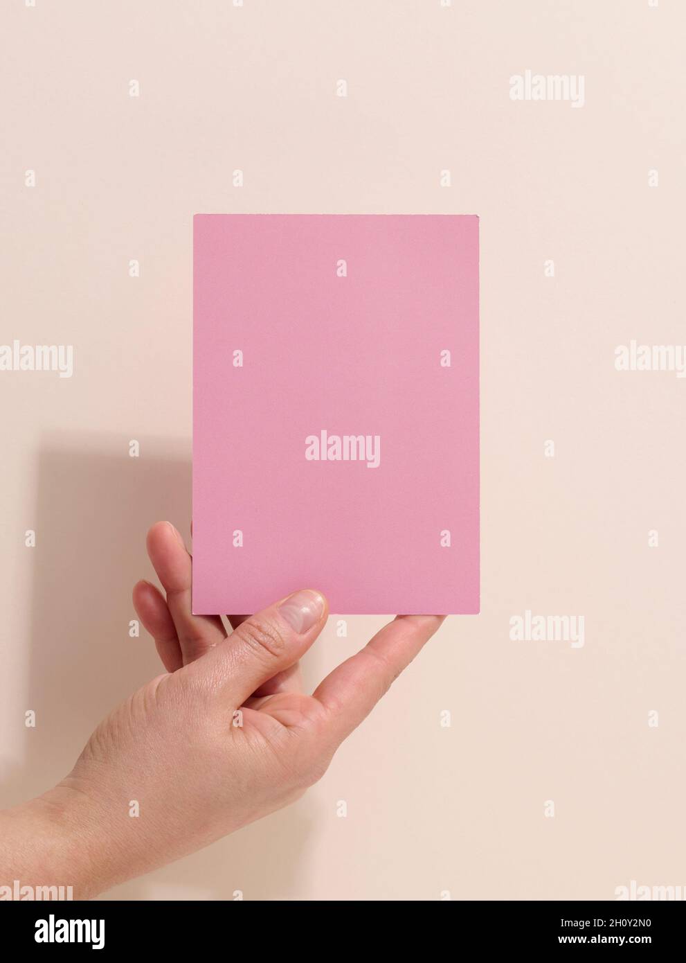 Weibliche Hand mit leerem rosa Papier auf beigem Hintergrund. Kopieren Bild oder Text einfügen, Nahaufnahme Stockfoto