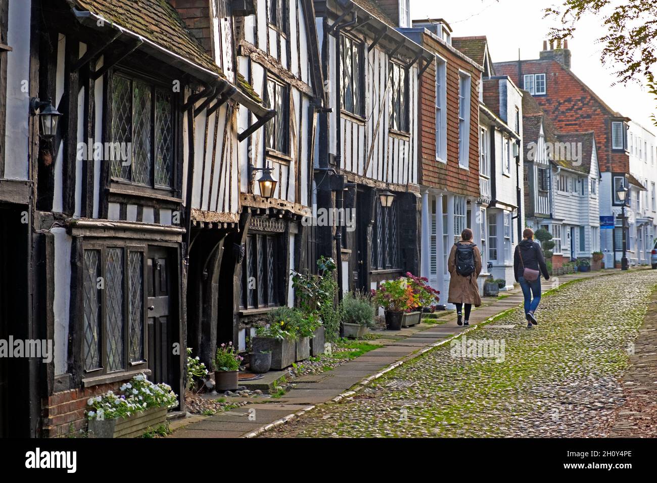 Rückansicht von zwei Frauen, die auf einer gepflasterten Straße an mittelalterlichen Fachwerkhäusern in der Stadt Rye vorbeigehen East Sussex England Großbritannien Großbritannien GROSSBRITANNIEN KATHY DEWITT Stockfoto