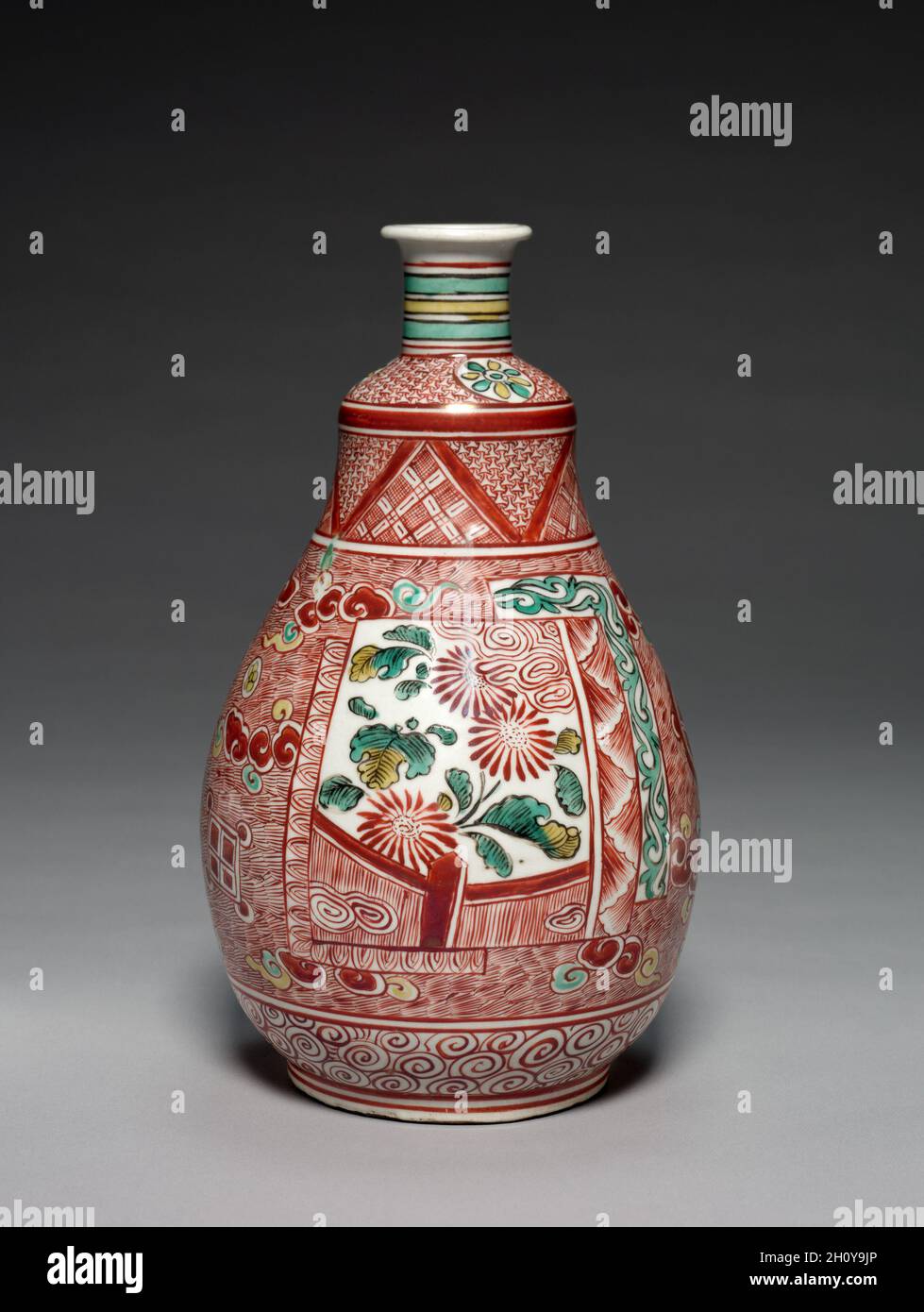 Tee-Sake-Flasche in Whiskform, 1660er bis Anfang 1670er Jahre. Japan, Edo-Zeit (1615-1868). Porzellan mit Emaille-Glasur (Hizen-Geschirr, Kakiemon-Typ, Ko-Kutani-Stil); insgesamt: 25.4 x 14.7 x 14.7 cm (10 x 5 13/16 x 5 13/16 Zoll). Diese Sake-Flasche ähnelt einem Schneebesen, der bei der Zubereitung von pulverförmiges grünem Tee verwendet wird, wobei der Griff oben und der Bürstenkörper unten aufflackert. Sein kühnes Design wird durch Bilder von Chrysanthemen und Granatäpfeln in Paneelen auf einem Boden aus roten Schraffuren mit dreifarbigen Wolken verankert. Zusätzliche Muster aus Wirbeln, Streifen, Blumen und anderen Formen machen das Stück zum Blickfang Stockfoto