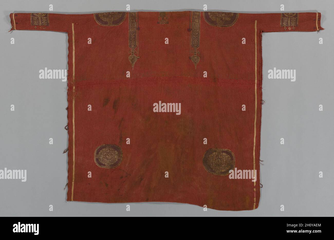 Luxuriöse Woolen Tunika mit dekorierten Bändern und Rundeln, 600s-700s. Ägypten, Umayyaden-Zeit (661–750). Leinwandbindung mit Schlitz- und Schwalbenbindung, zusätzliche Schussverpackung, Stickerei; ungefärbtes Leinen, gefärbte Wolle; Insgesamt: 205 x 170.2 cm (80 11/16 x 67 Zoll). Seit Mitte des 20. Jh. n.Chr. waren Tuniken die wichtigsten Kleidungsstücke in Ägypten. Diese Unisex-Tunika ist auf der Vorder- und Rückseite mit den gleichen geometrischen und figürlichen Motiven verziert, darunter Männer auf der Pferdejagd und geometrische geflochtene Knoten, die den Träger vor Schaden schützen sollten. Ein roter Hintergrund wurde im frühen Ich bevorzugt Stockfoto