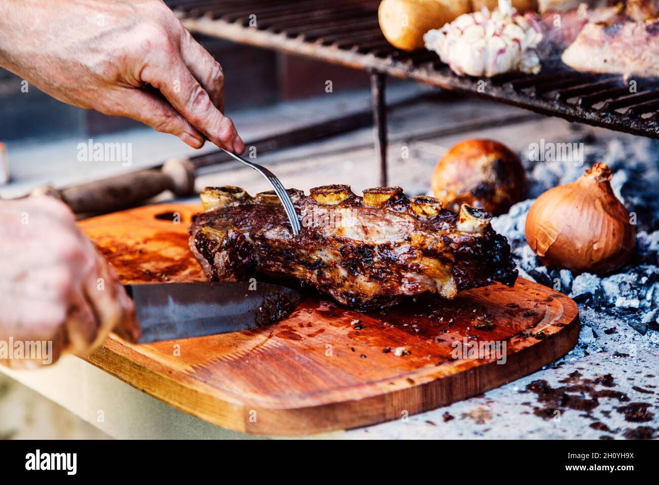 Argentinischer Mann schneidet Roastbeef-Rippchen. Traditionelles Asado aus Argentinien. Grill. Stockfoto