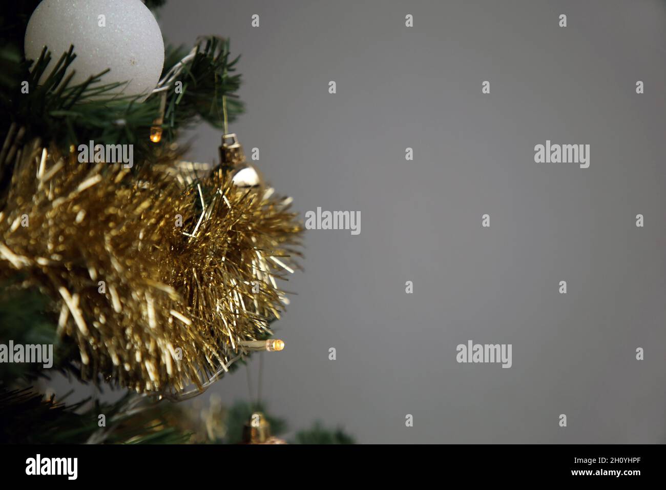 Nahaufnahme eines grünen Weihnachtsbaums mit goldenen, weißen und silbernen Ornamenten sowie kleinen dekorativen Lichtern. Grauer Hintergrund. Fröhliches und fröhliches Farbbild. Stockfoto