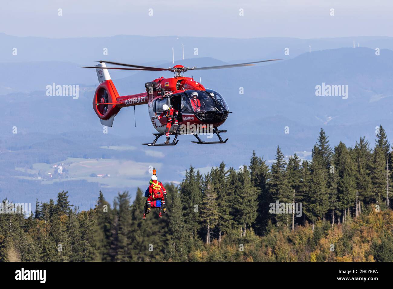 Waldkirch, Deutschland. Oktober 2021. Je ein Mitglied der Bergwacht und der DRF Luftttung hängt unter einem Rettungshubschrauber an einem Seil, während im Hintergrund der Schwarzwald zu sehen ist. Während des Seilbahntrainings übt die Besatzung der Freiburger Station der DRF Luftttung (Rufzeichen Christoph 54) zusammen mit dem Schwarzwälder Bergwacht den Einsatz mit der Winde unter einem Hubschrauber. Kredit: dpa/Alamy Live Nachrichten Stockfoto