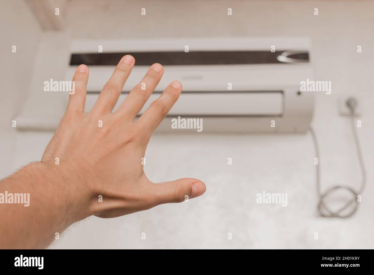 Der Typ legt seine Hand unter die Klimaanlage im Zimmer, um die Temperatur und das Gefühl von warmer oder kalter Luft zu überprüfen. Stockfoto