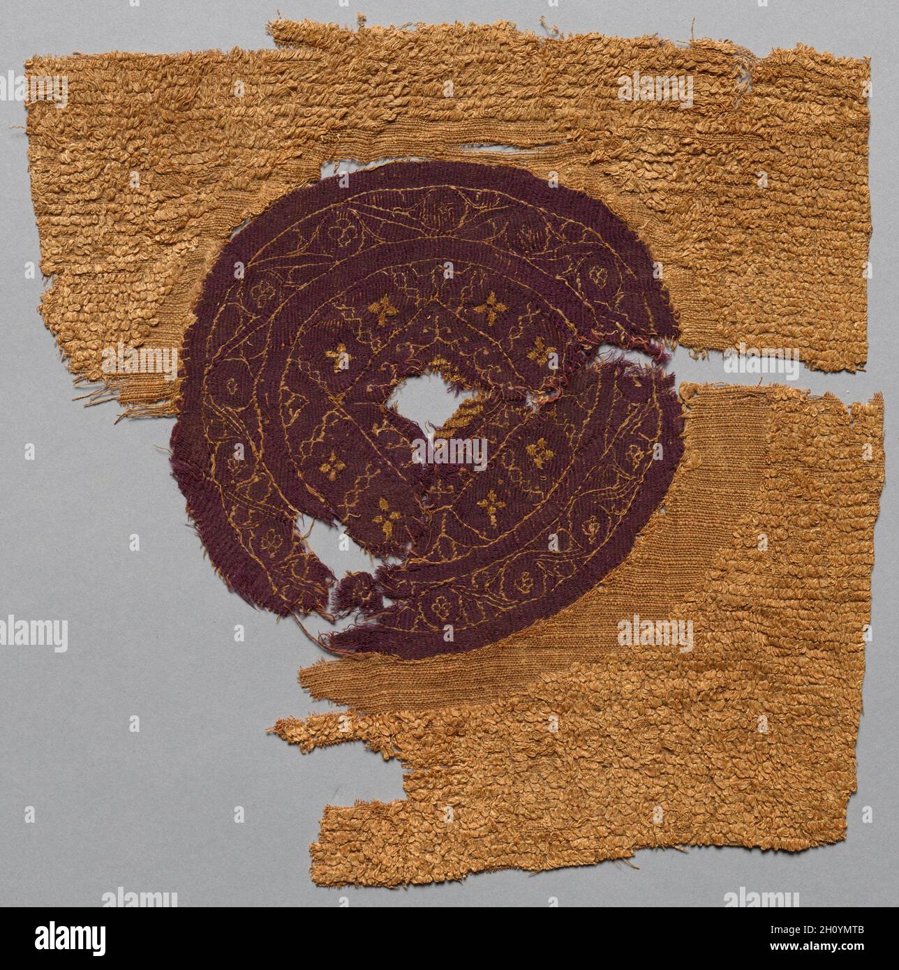 Fragment mit Goldfolie, aus einem Möbelstoff, 300s-400s. Ägypten, byzantinische Zeit, 4.-5. Jahrhundert. Ungefärbtes Leinen, gefärbte Wolle und Goldfolie; Leinwandbindung mit ergänzenden Schussschlaufen, Spaltteppich-Webart mit ergänzender Schussverpackung; insgesamt 26.1 x 25.2 cm (10 1/4 x 9 15/16 Zoll). Die seltene Goldfolie und die reichhaltige violette Wolle in diesen beiden Fragmenten angereicherten ursprünglich einen luxuriösen Stoff. Die kostbare Goldfolie, die um einen Seidenkern gewickelt ist, bildet das zentrale Motiv in einem Diamanten, der in Tapisserie-Gewebe gewebt ist. Die umschließende Knotenkonstruktion – erreicht mit drei überlappenden Quadraten (im kleinen Fr. Stockfoto