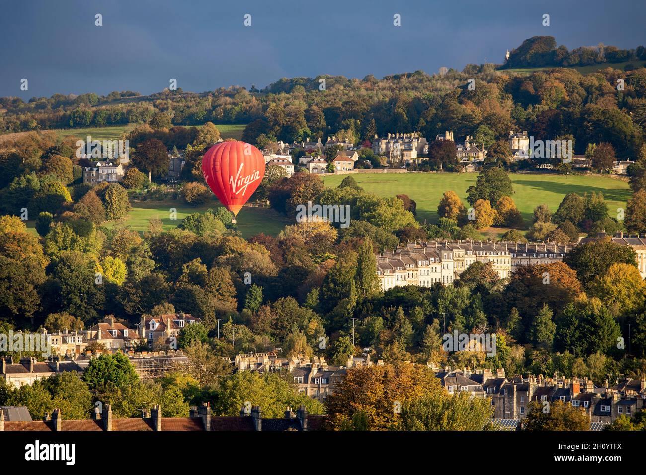 BATH, UK - 14. OKTOBER 2021 : An einem sonnigen Herbstmorgen hebt Ein Heißluftballon der Marke Virgin vom Royal Victoria Park ab. Stockfoto