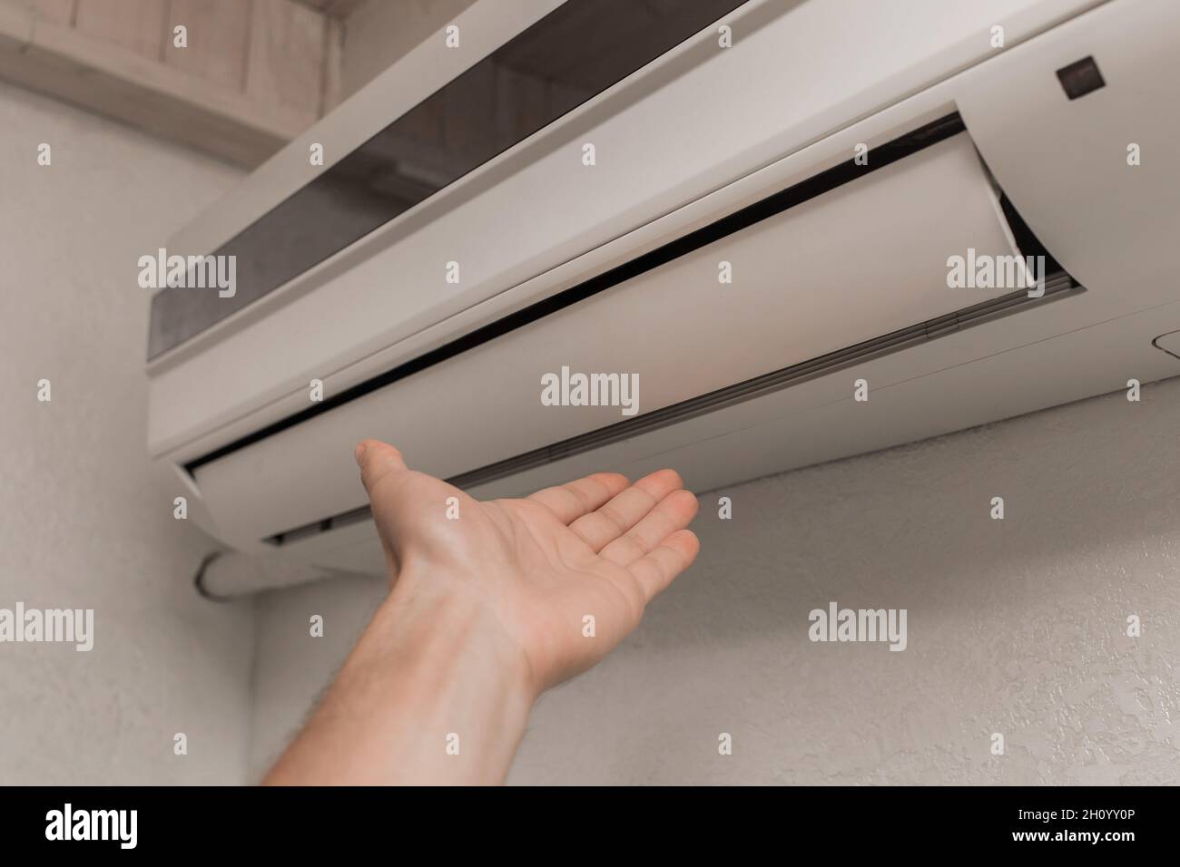 Der Typ legt seine Hand unter die Klimaanlage im Zimmer, um die Temperatur und das Gefühl von warmer oder kalter Luft zu überprüfen. Stockfoto
