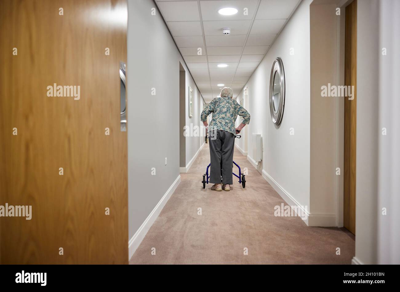 Rückansicht Einer Älteren Frau Mit Walker, Die Im Altersheim Den Korridor Entlang Läuft Stockfoto