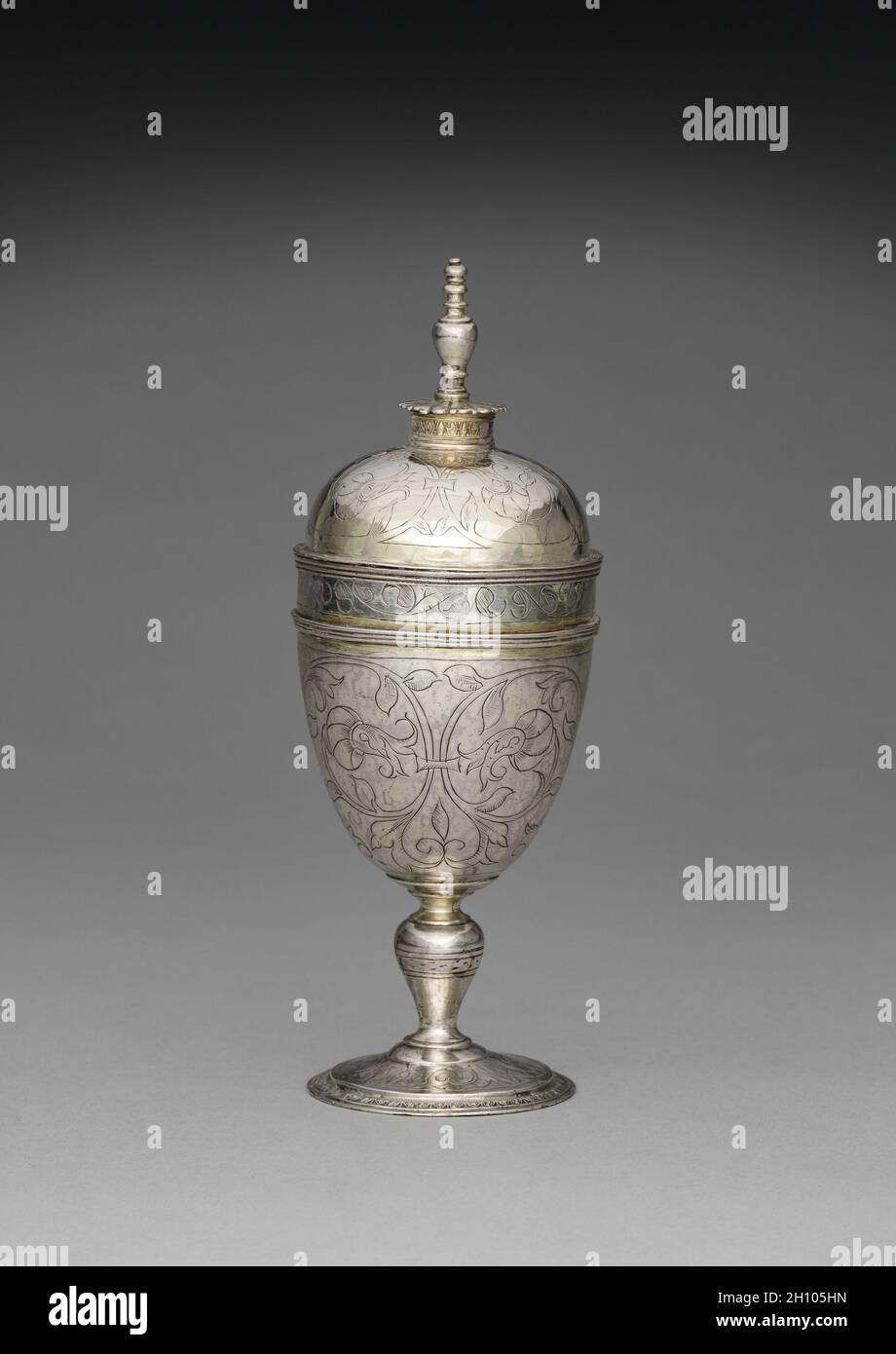 Standbecher und Abdeckung, 1593. London, England, Ende des 16. Jahrhunderts. Silber, teilweise vergoldet; insgesamt 19.3 x 7.4 cm (7 5/8 x 2 15/16 Zoll). Dieses Gefäß, das in den letzten Jahren der Tudor-Dynastie (1485–1603) hergestellt wurde, veranschaulicht die symmetrischen Muster, horizontalen Designs und die klare Raumaufteilung, die für die englische Silberarbeit der damaligen Zeit typisch waren. Die funktionale Form und die dekorativen Designs, die für stehende Tassen charakteristisch sind, machten sie ideal für zeremonielle Anlässe. Stockfoto