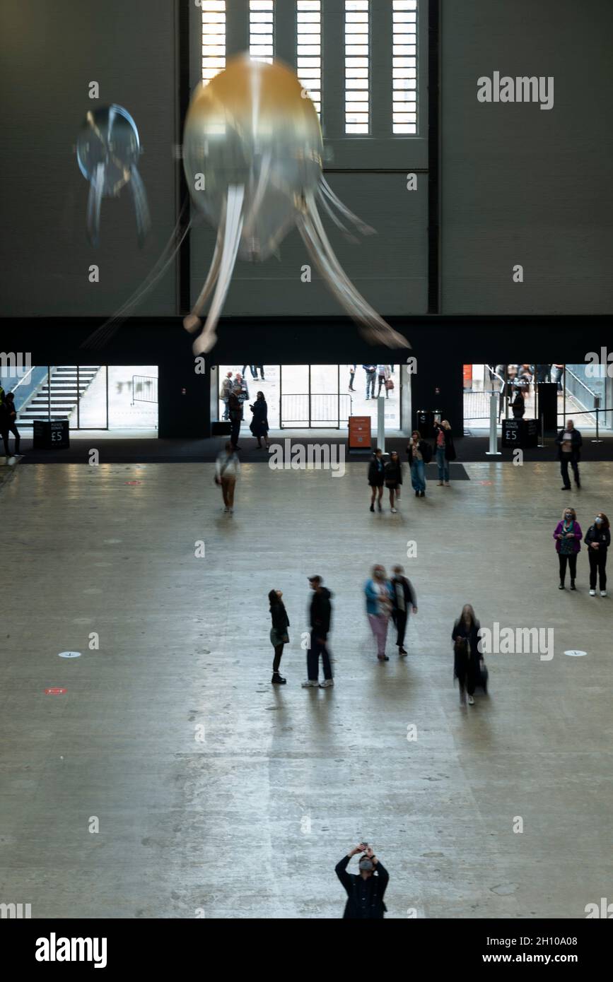 London, Großbritannien. Oktober 2021. Die Besucher sehen schwebende Kunstflugkörper, die Anicka Yis neues Luftwerk „in Love With The World“ bilden, in der Turbine Hall of Tate Modern für die Hyundai-Kommission 2021. Die Installation besteht aus Maschinen, die als Kunstflugkörper bezeichnet werden, basierend auf Lebensformen des Ozeans und Pilzen, die in der Luft schweben, und stellt eine Neueinbildung dar, wie künstliche Intelligenz und neue Maschinen die Welt bewohnen könnten. Die Arbeit kann bis zum 16. Januar 2022 erlebt werden. (Langzeitbelichtung). Kredit: Stephen Chung/Alamy Live Nachrichten Stockfoto