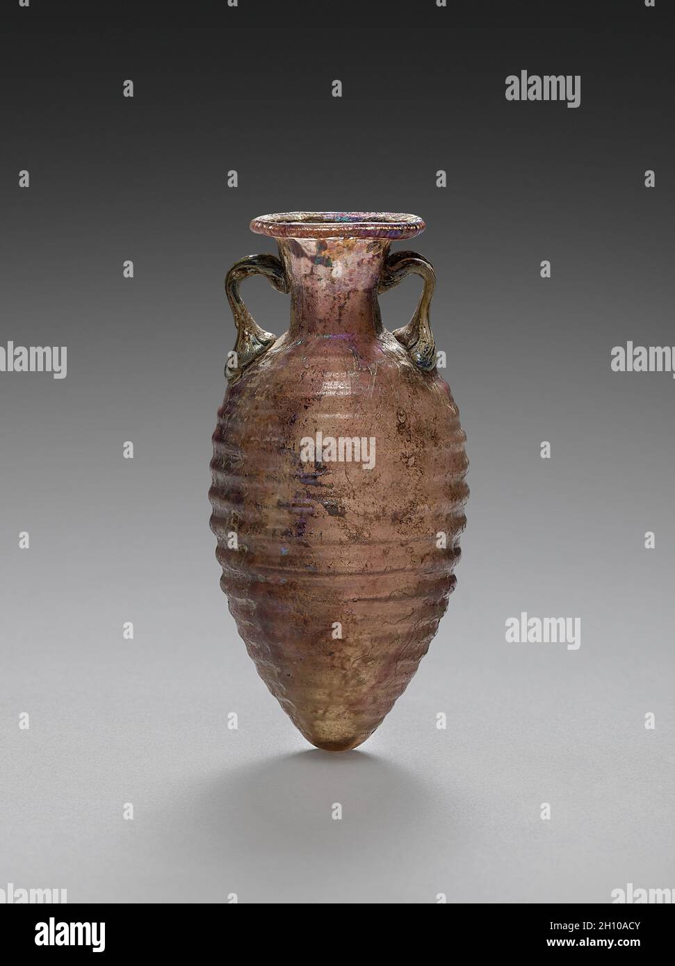 Amphoriskos (kleine Amphora), AD 50-100. Roman. Glas, formgeblasen; Durchmesser: 2.5 cm; insgesamt: 7.5 x 3.5 cm (2 15/16 x 1 3/8 Zoll). Zuerst in einer Form geblasen, dann mit separat hergestellten Griffen geliefert, hielt dieses kleine Gefäß wahrscheinlich parfümiertes Öl, ein wertvolles gut. Ursprünglich violett gefärbt, ist seine Oberfläche jetzt teilweise durch Bereiche mit Biff und schillernder Verwitterung getrübt. Der fein gerippte Korpus ist jedoch sehr elegant, und seine extravagante moderne Box zeugt von seinem bedeutenden Wert für einen modernen Besitzer (vor 1919). Stockfoto